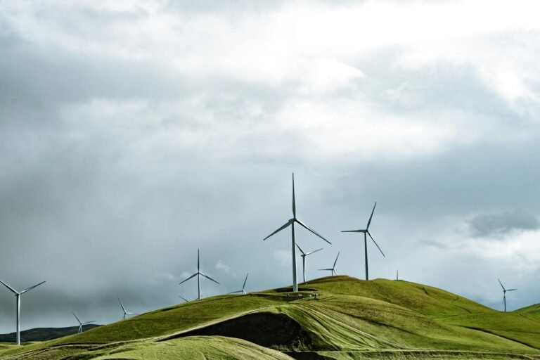 Wind turbines on lush hills with a dramatic cloudy sky, symbolizing clean energy and sustainability.